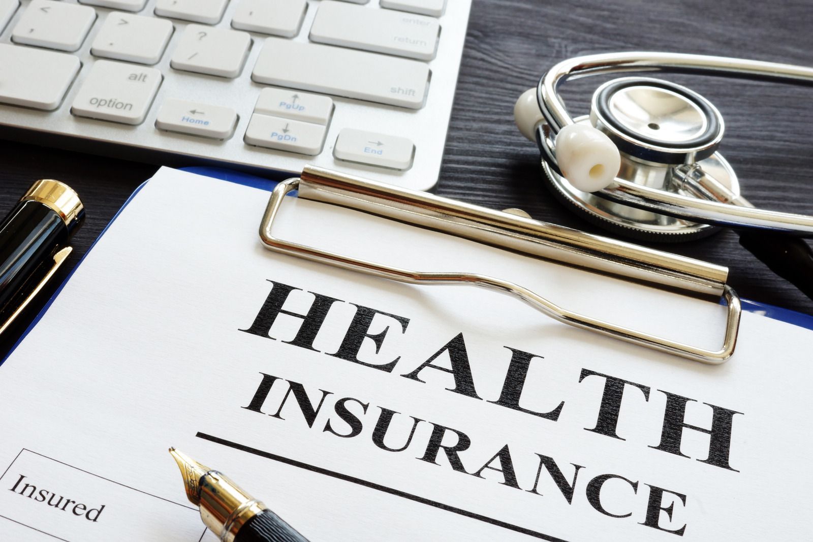 Health insurance document on desk with pen, keyboard, and stethoscope