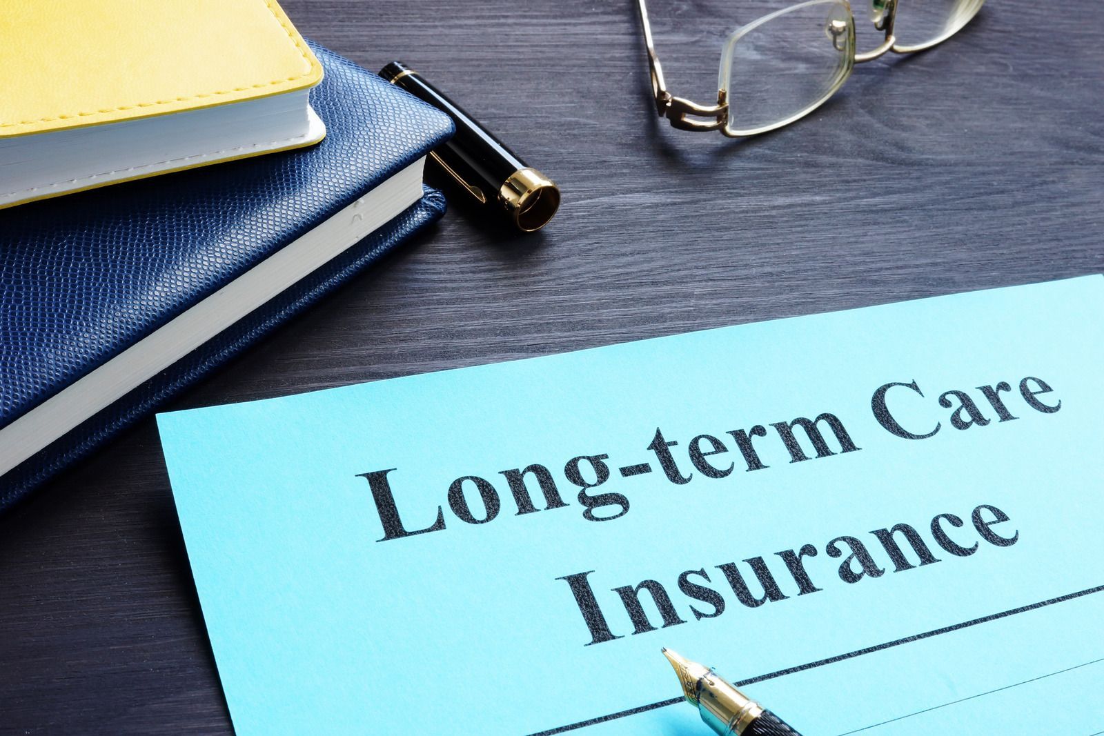 Long-term care insurance document on desk with notebook and glasses