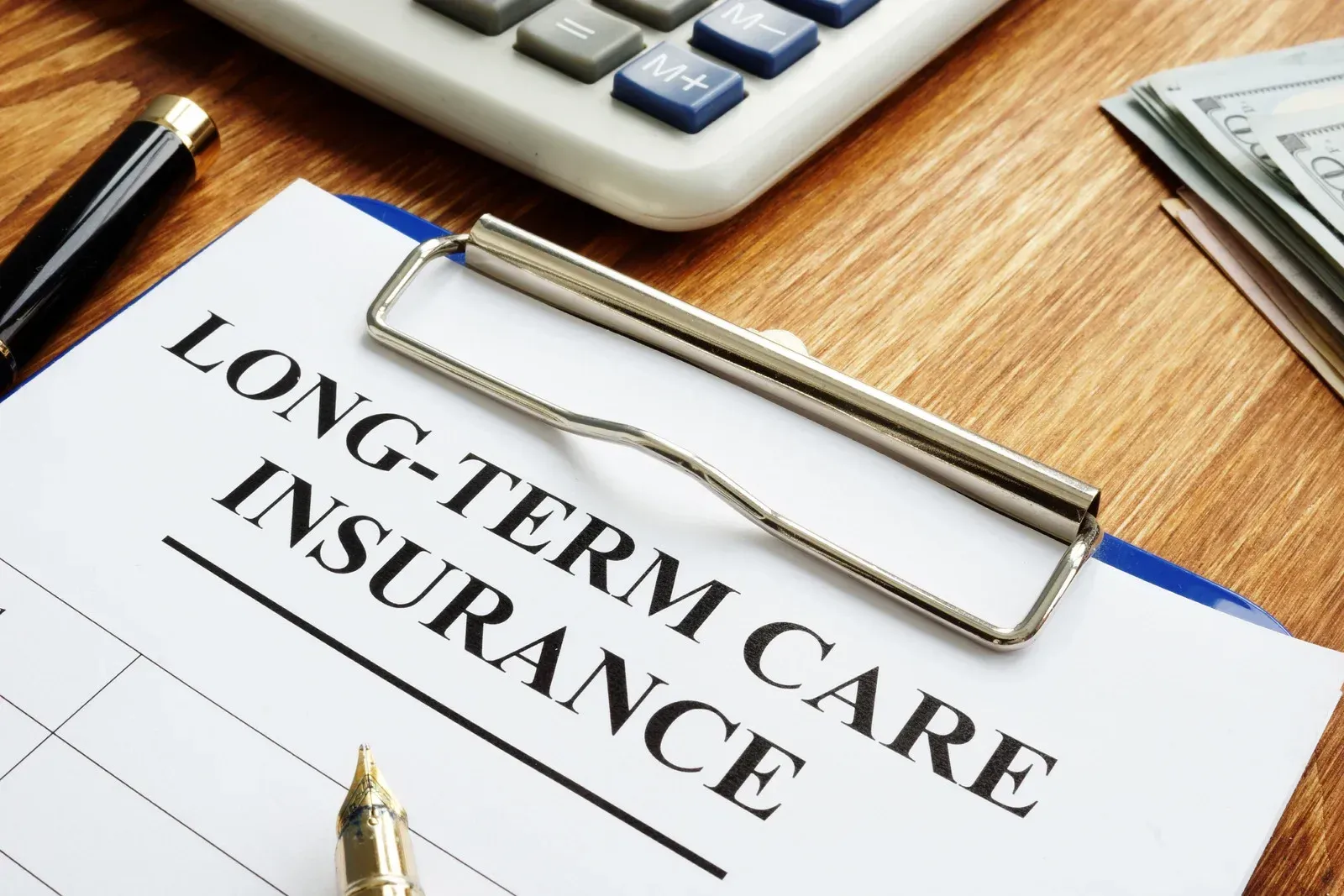 Long-term care insurance form on desk with clipboard, calculator, and stack of money