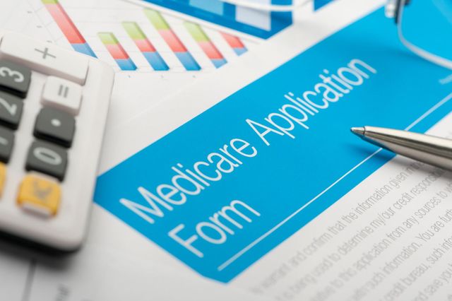 Medicare application form on a desk with calculator and pen, blue form visible