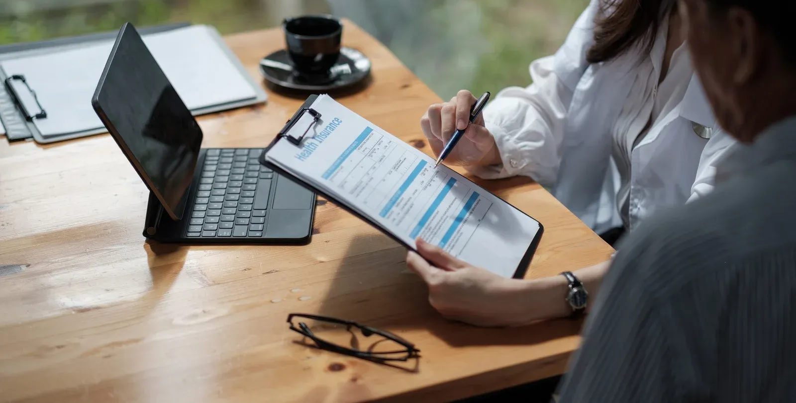 Two people reviewing a tablet with charts at a wooden desk beside a laptop and coffee cup
