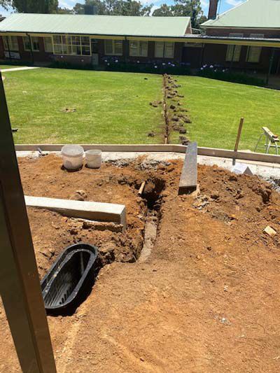 A drain is being installed in the dirt in front of a house.