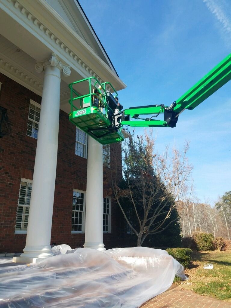 A green lift is extending to a white building's pillars, painting exterior.