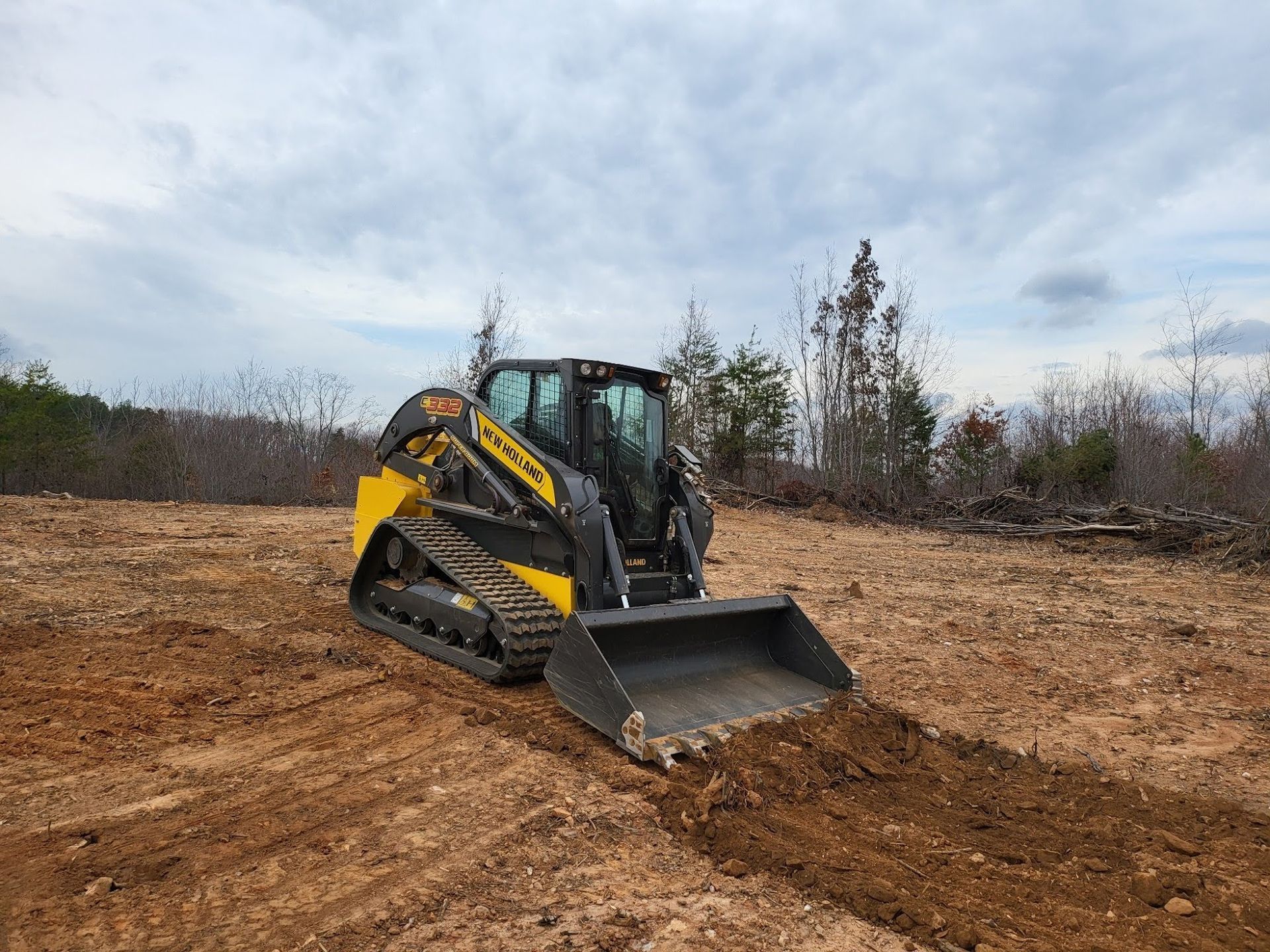 Yellow and black skid steer digging into dirt in an open field under a cloudy sky.