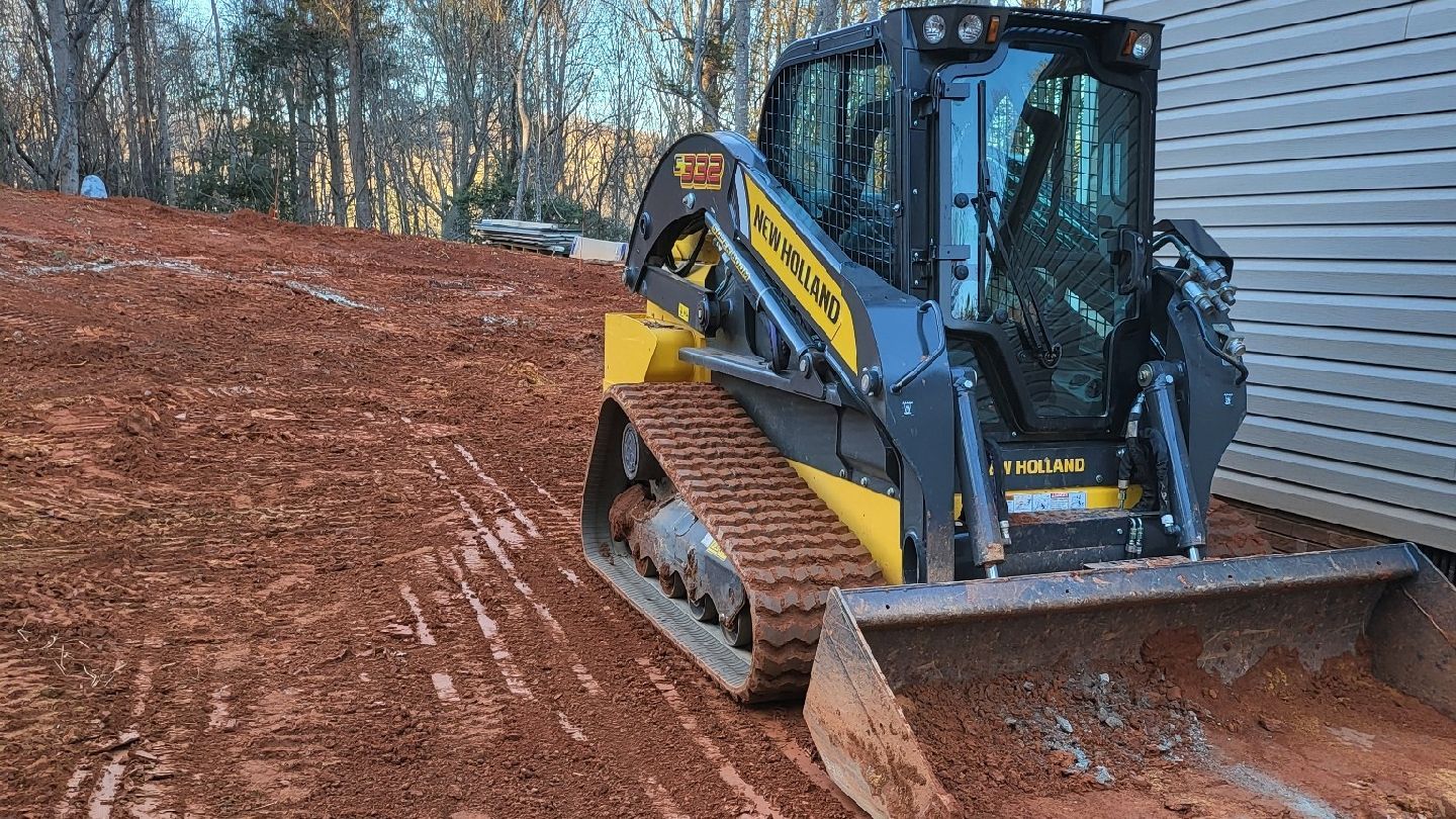 Yellow and black track loader on a dirt hill, likely for construction.