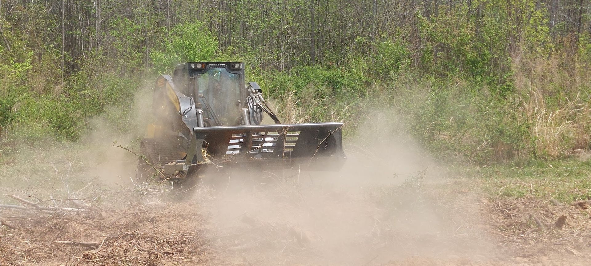 A tractor with a brush cutter is creating dust while clearing brush.