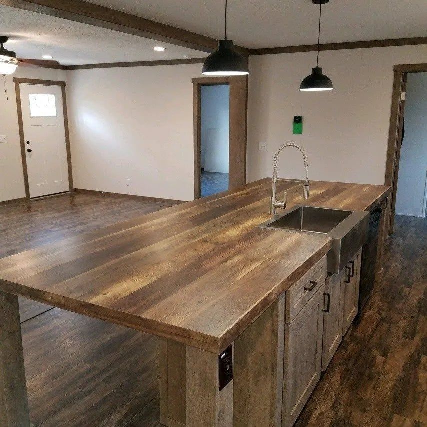 Kitchen island with a wooden countertop and a stainless steel sink, with overhead lighting.