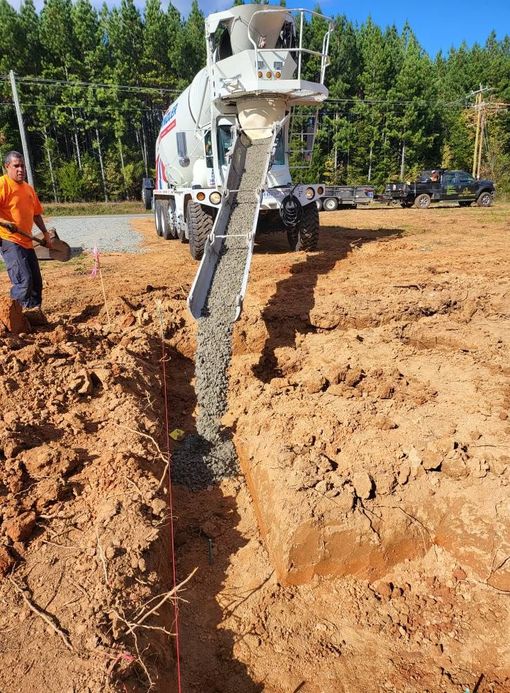 Yellow skid steer on red dirt next to a light beige house.
