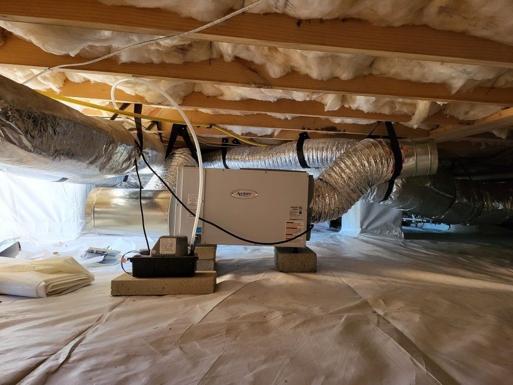 Dehumidifier unit installed in a crawlspace, with flexible ducting and insulation visible.