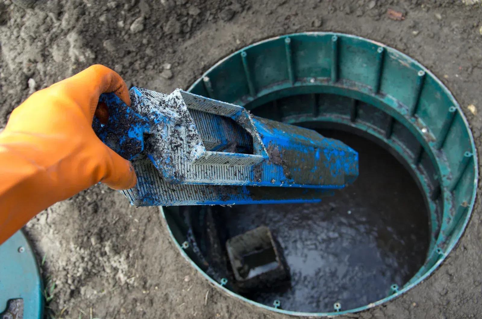 Person in orange glove removing filter from septic tank access point.