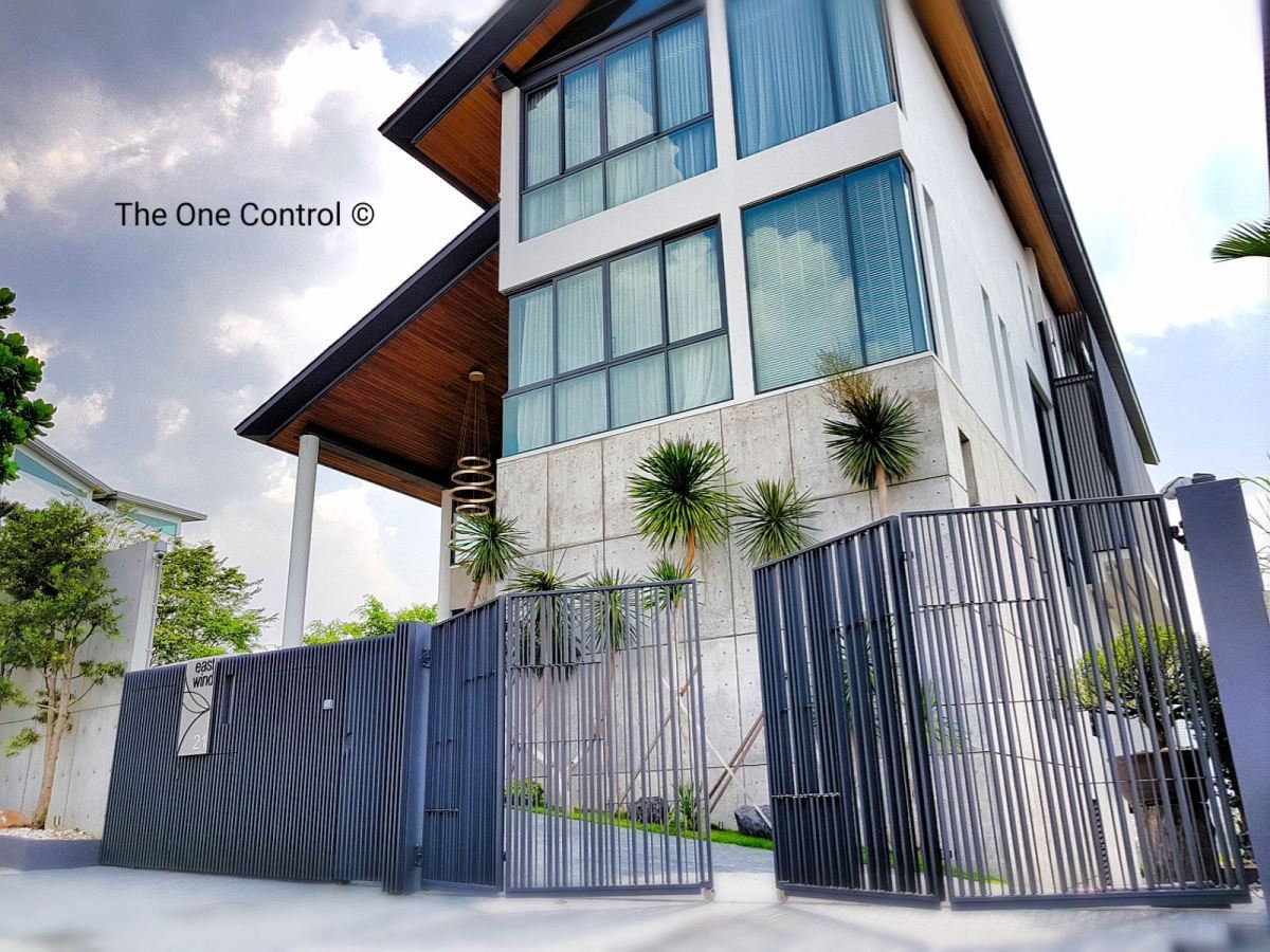 A modern three-story home with a grey vertical-slat folding autogate at the entrance