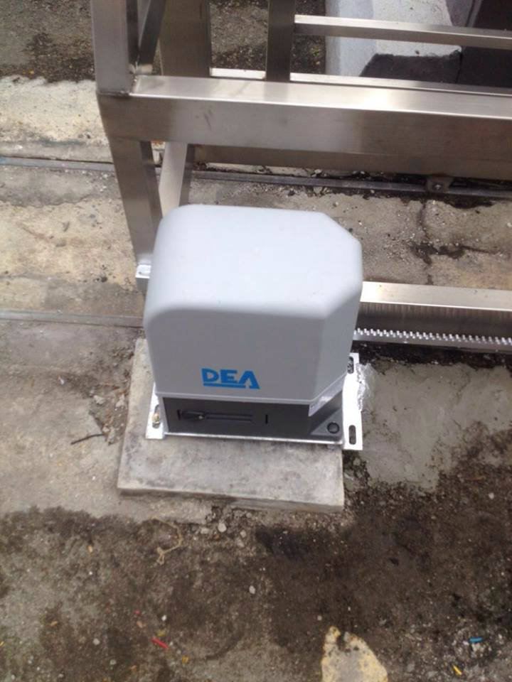 A grey and black DEA autogate motor system installed next to a stainless steel sliding gate.