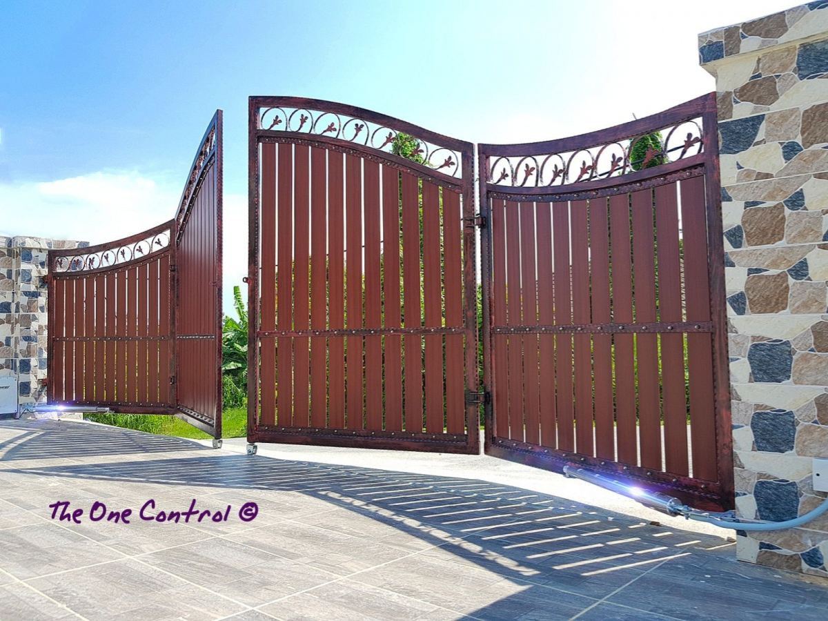 An ornate stainless steel residential gate next to a brick wall with a car in the foreground