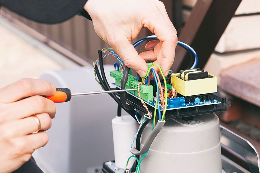 A technician using a screwdriver to fix electrical wiring on a gate motor during professional autoga