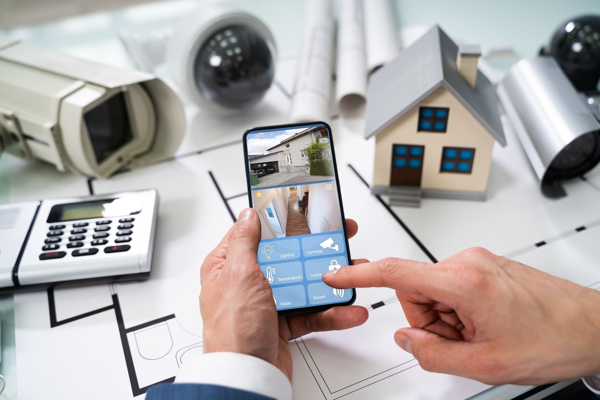 Person holding a smartphone displaying a home wireless alarm security app next to security cameras a
