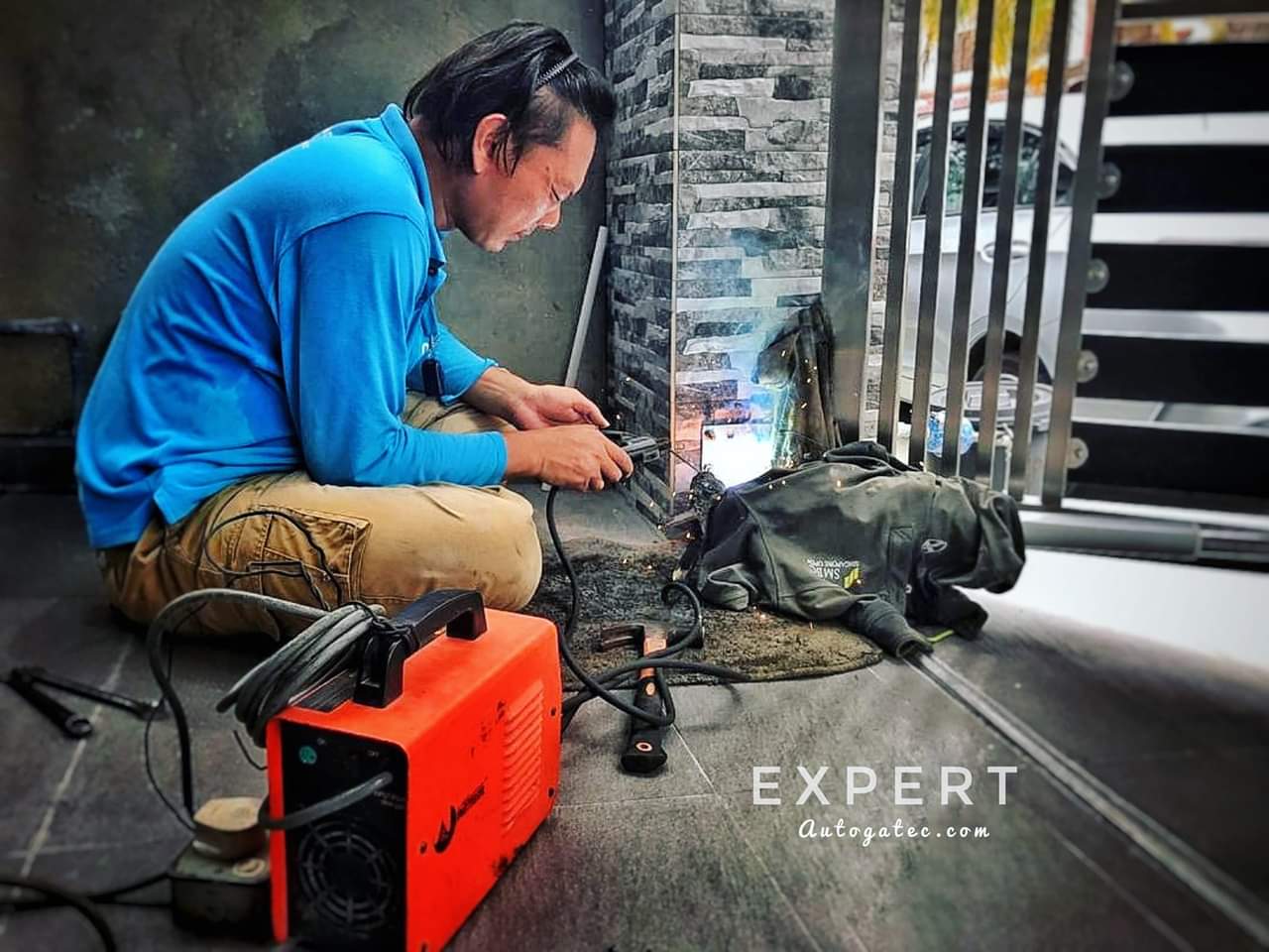 A technician welding a gate component next to a tiled pillar using an orange welding machine