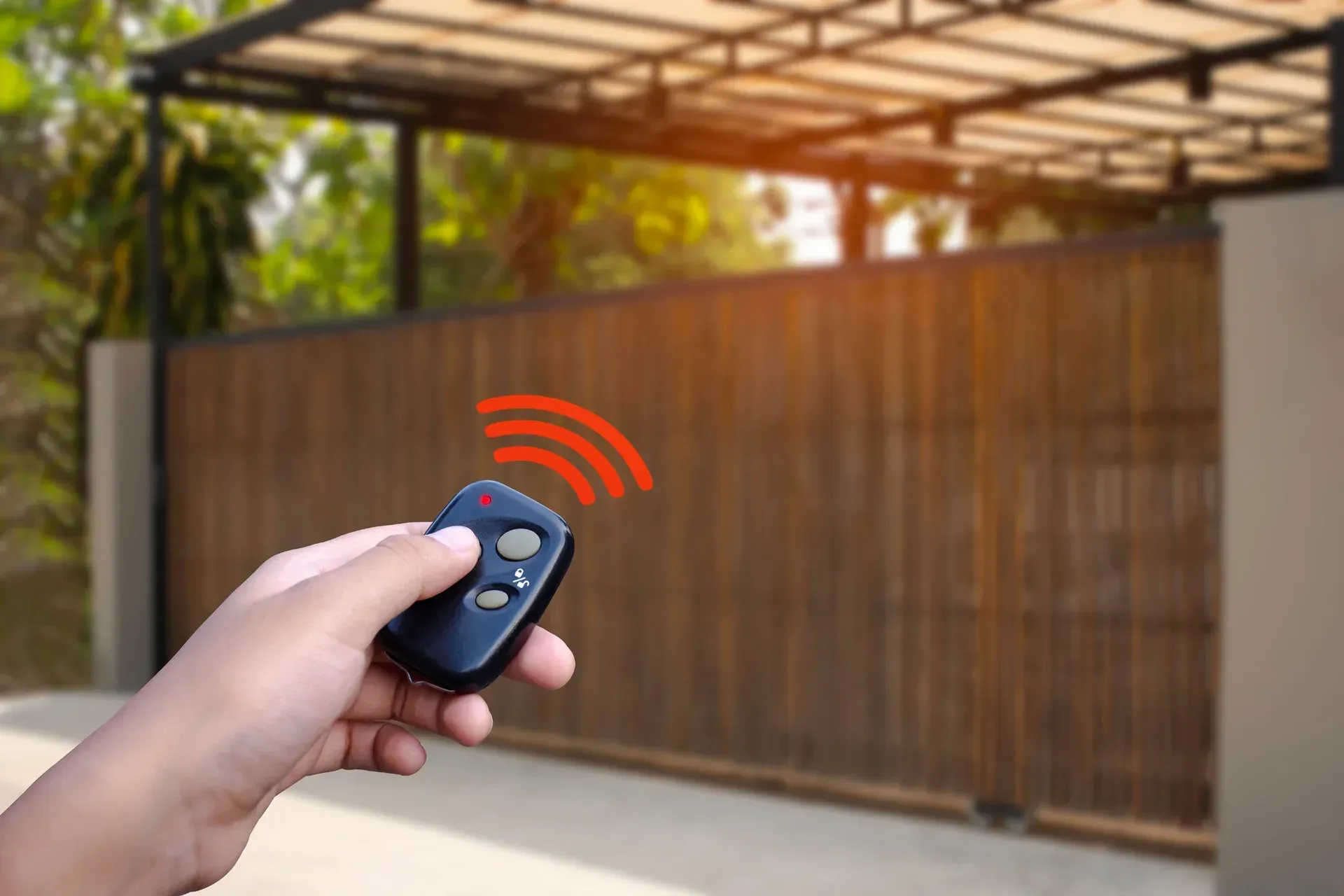 Hand pressing a remote control to operate a home autogate system Malaysia house entrance.