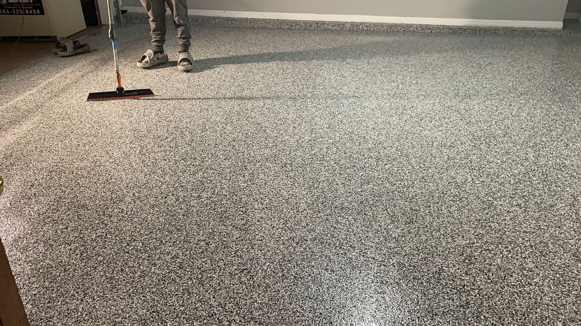 A man is cleaning a garage floor with a broom.