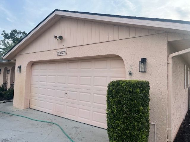A house with a pink garage door and a bush in front of it.