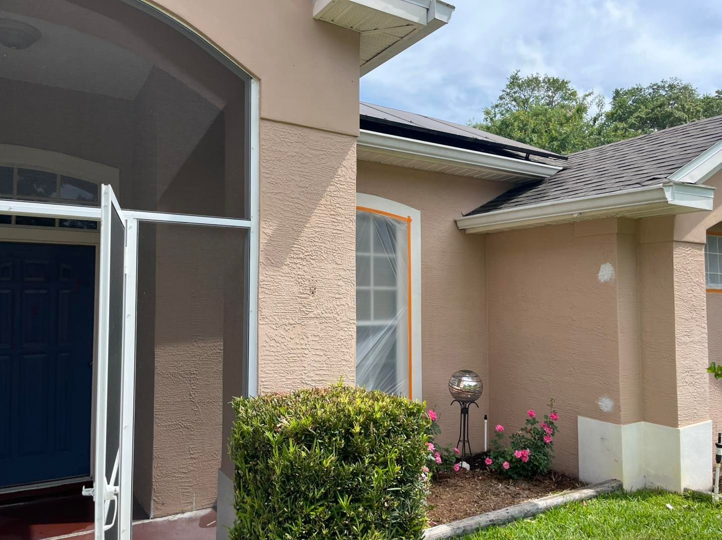 A house with a screened in porch and a bush in front of it.