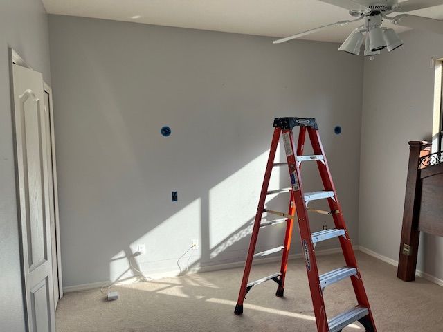 A room with a painted gray wall; an orange ladder stands before it. Blue marks show where something will be installed.