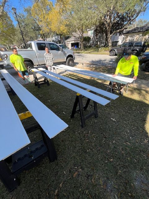 Three people working on white boards outdoors, setting them on saw horses.