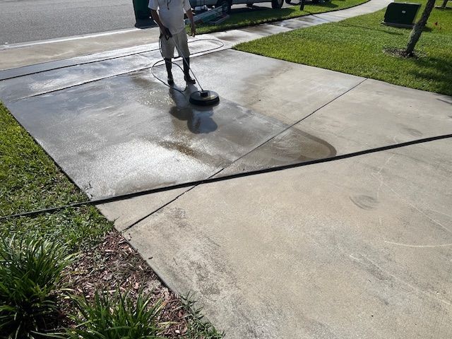 Person power washing a concrete driveway with a spinning surface cleaner.