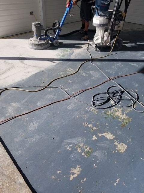 Person grinding a concrete surface with two machines, removing old paint, outdoors.