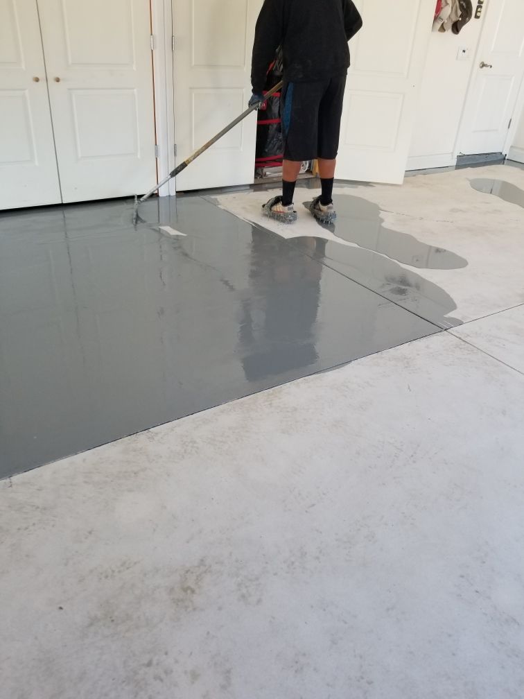 Person applying gray epoxy coating to a garage floor with a long roller.