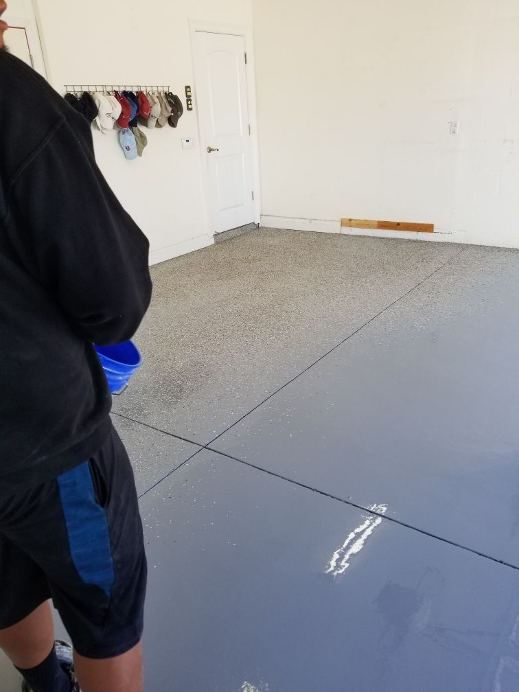 Person pouring blue coating on a garage floor. The floor is partially covered in gray and blue coating.