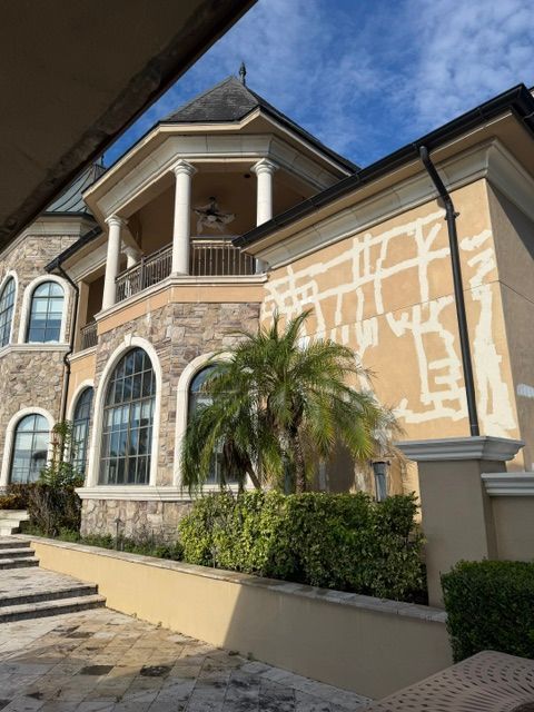 Luxury house exterior with arched windows, balcony, and palm tree beside a paved walkway