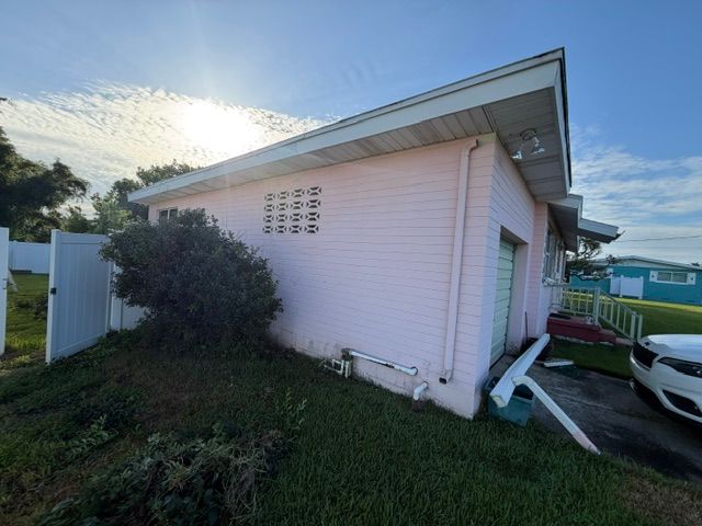 Side view of a white house with a slanted roof, grassy yard, and parked cars at sunset