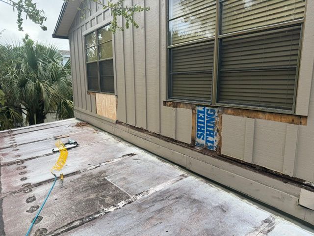 Rooftop beside a tan house with windows, vents, and a blue tape measure on the weathered surface.