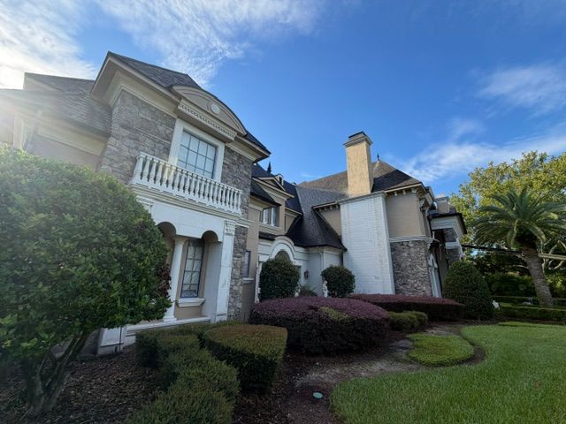 Large white two-story house with balcony, landscaped front yard, and blue sky