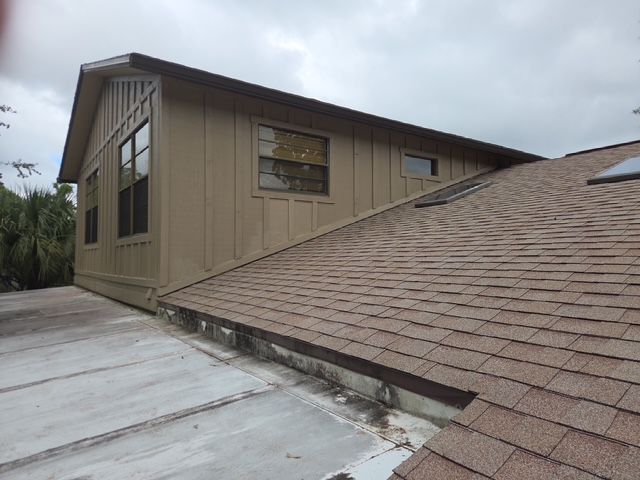 Sloped tan house roof with a flat roof section and windows under a cloudy sky