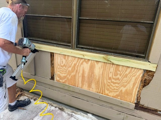 Person using a drill to install plywood across the lower exterior wall of a house