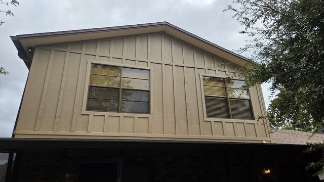 Two-story beige house exterior with windows and a dark lower porch roof