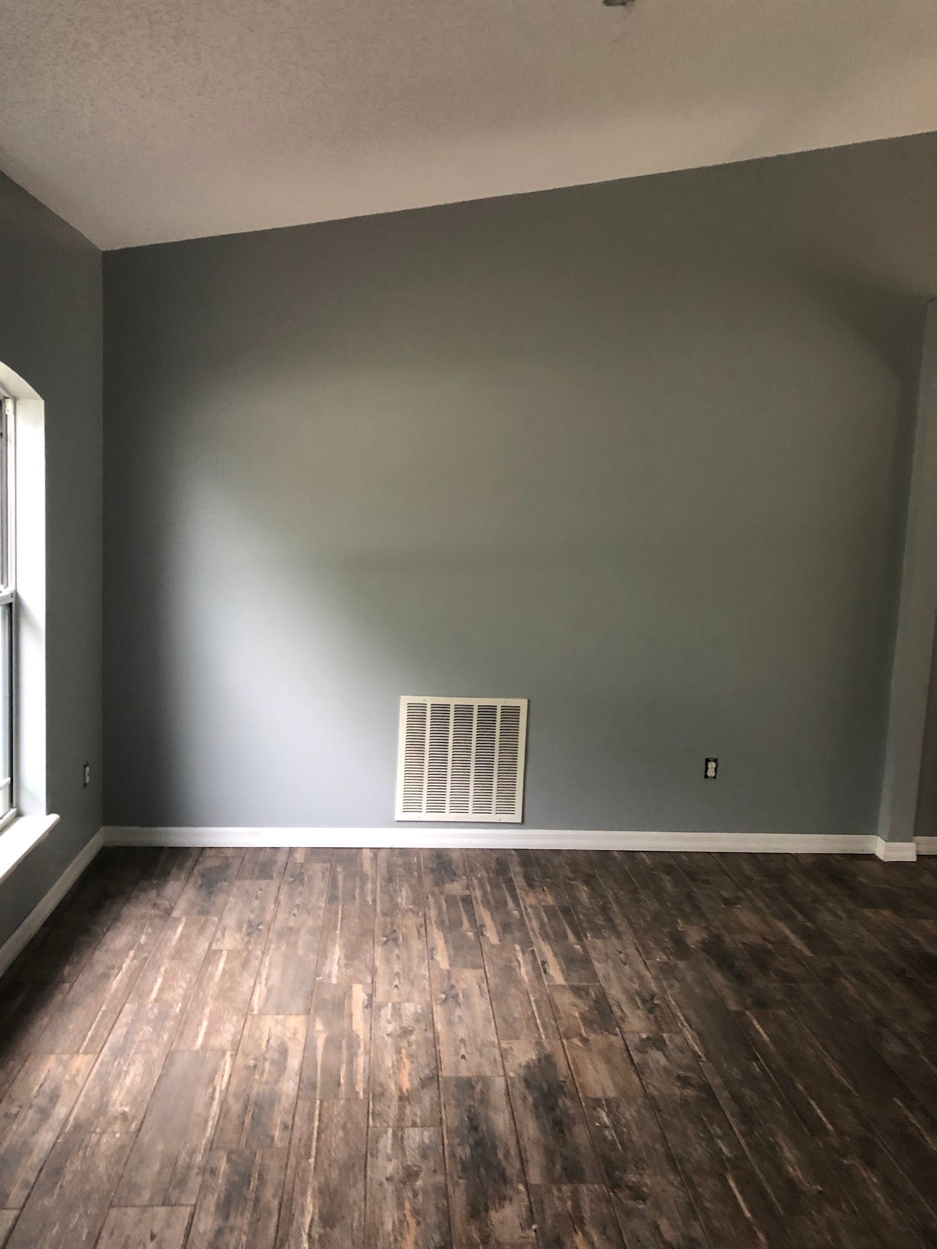An empty living room with a wooden floor and gray walls.