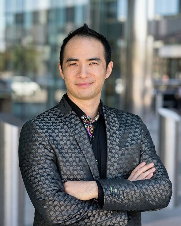 Person standing with arms crossed in a patterned jacket outdoors in front of a blurred building.
