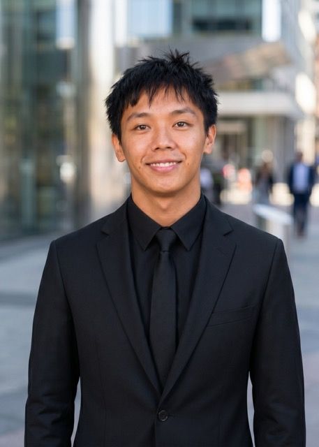 Person in a black suit standing outdoors on a city street, with a blurred urban background.