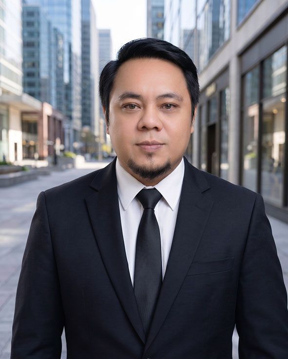 Man in a black suit and tie standing on a city street with tall buildings in the background