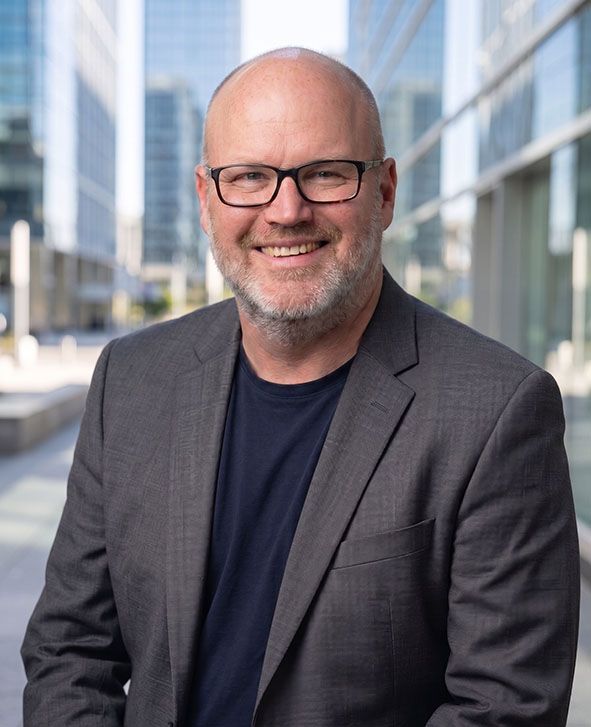 Smiling bald man in glasses and blazer standing outdoors in a modern city setting
