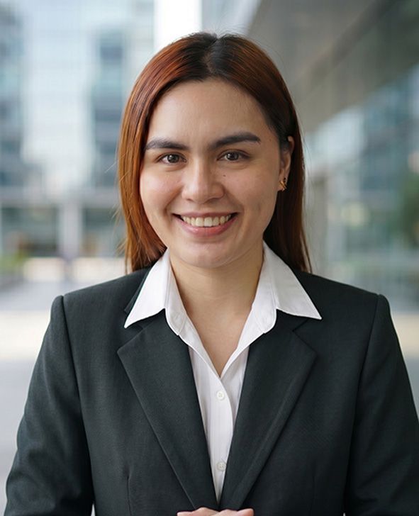 Smiling professional in a black blazer and white shirt, standing outdoors with blurred buildings behind.