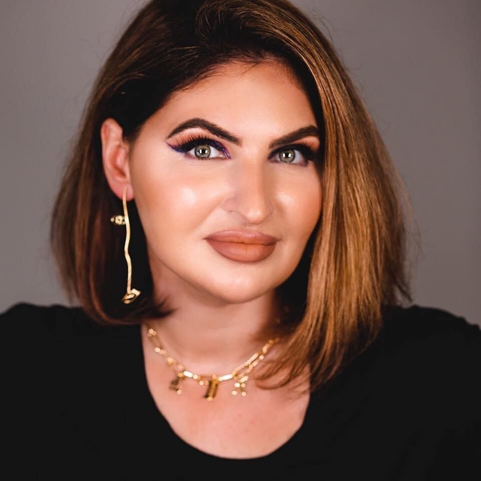 Portrait of a woman with shoulder-length brown hair, gold jewelry, and a black top against a dark background