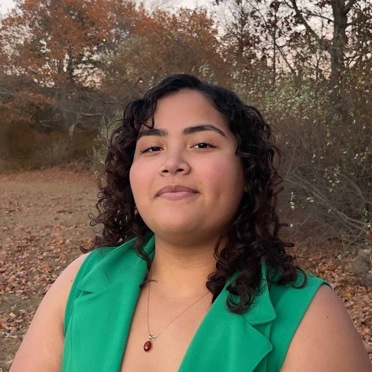 A woman wearing a green vest and a necklace is smiling for the camera.