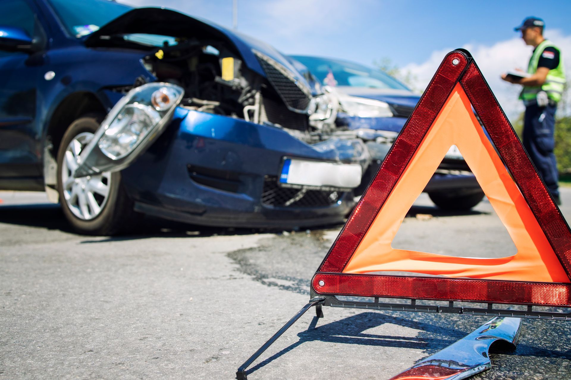 A woman is looking at her cell phone in front of a damaged car.