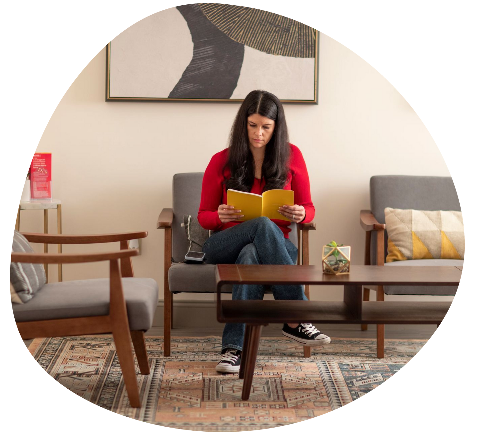 Woman in a red sweater reading a yellow book in a cozy living room with chairs and a coffee table