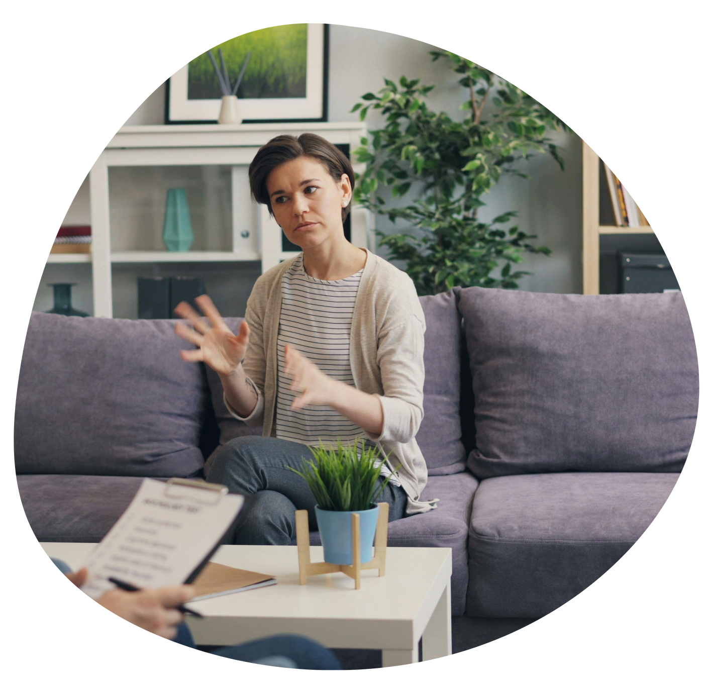 Woman speaking on a gray sofa in a bright living room, with a small table and plants nearby