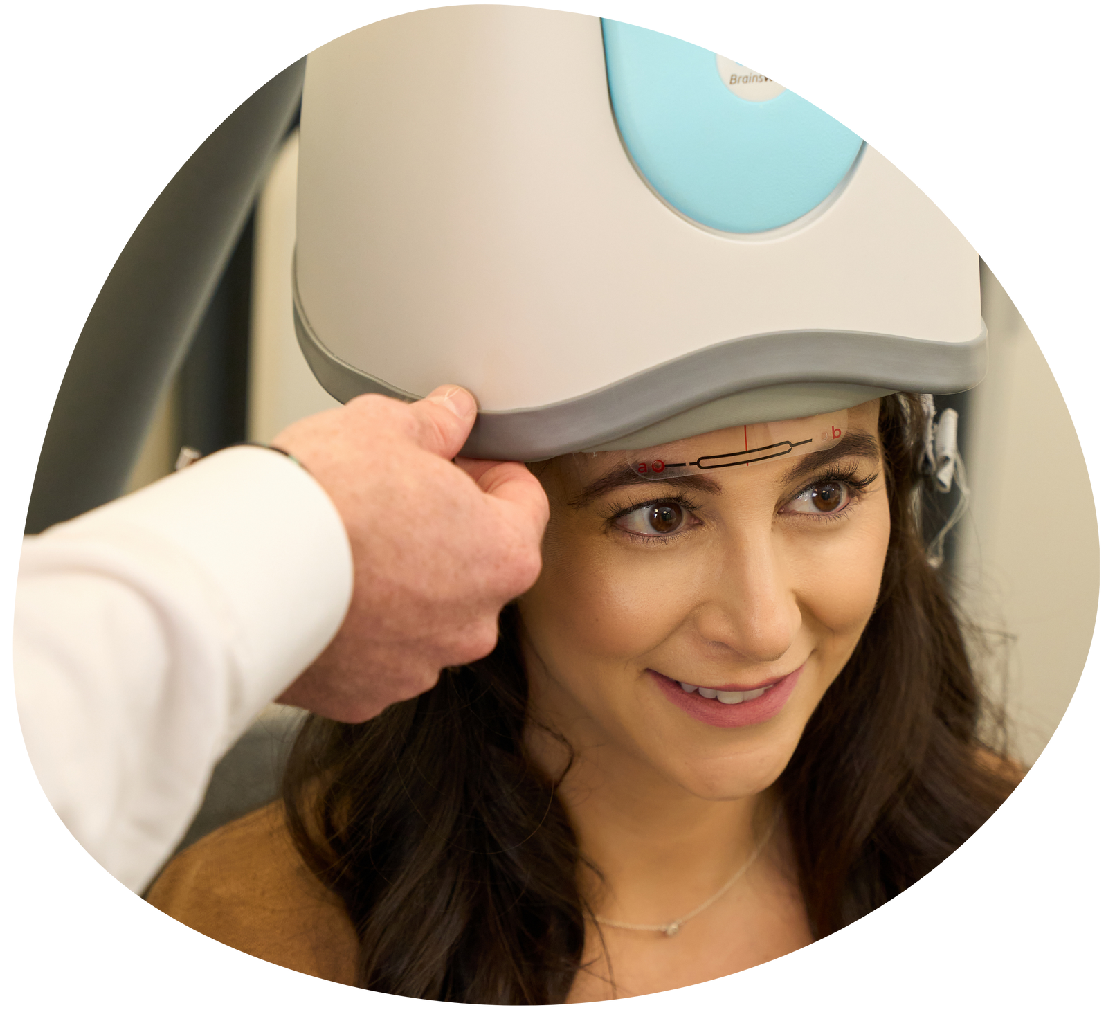Technician fitting a medical headpiece on a woman during a clinic exam