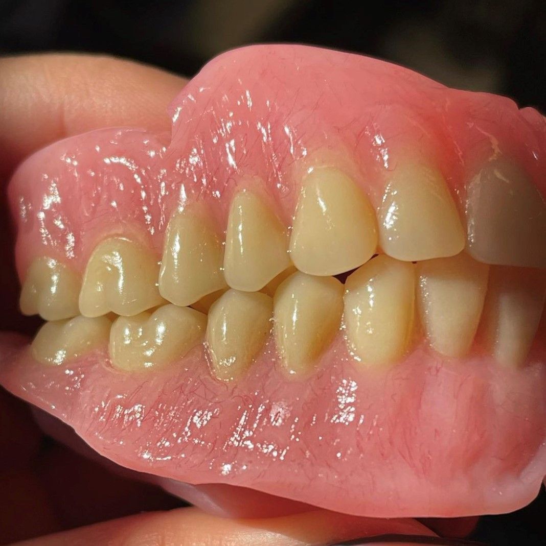 A person is holding a pink denture with white teeth.